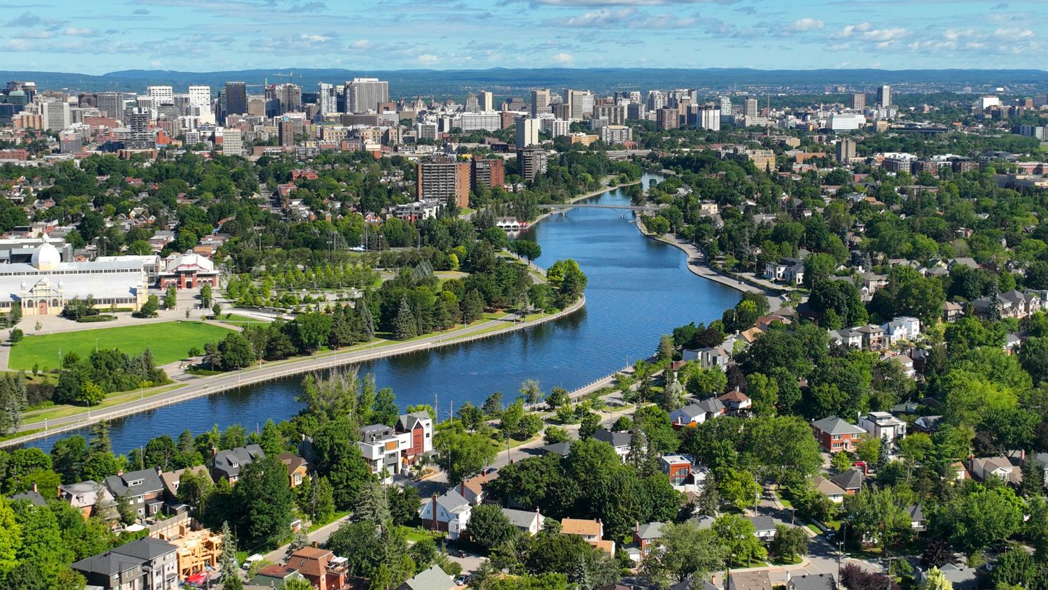 Aerial view of a city with a winding river through green parks and a mix of high-rise and residential neighborhoods.